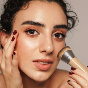 Woman applying foundation with complexion brush; brown bristles on beige ferrule