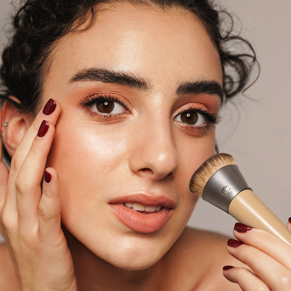 Woman applying foundation with complexion brush; brown bristles on beige ferrule