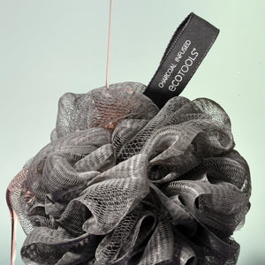 Charcoal bath sponge pouf hanging by a loop, dark gray mesh puff