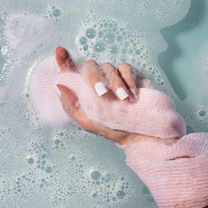 Pink exfoliating bath cloth held in foamy bath water