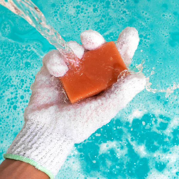 White textured bath glove with green cuff holding soap bar in water splash.