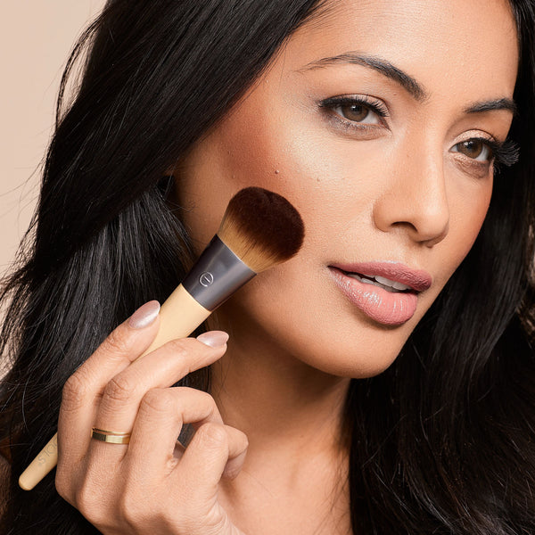 Woman holding a makeup brush near her cheek with visible highlight dots on skin