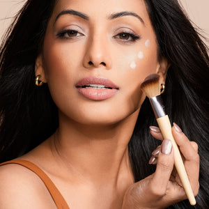 Woman applying makeup blush and highlighting with a tapered brush on cheek and temple
