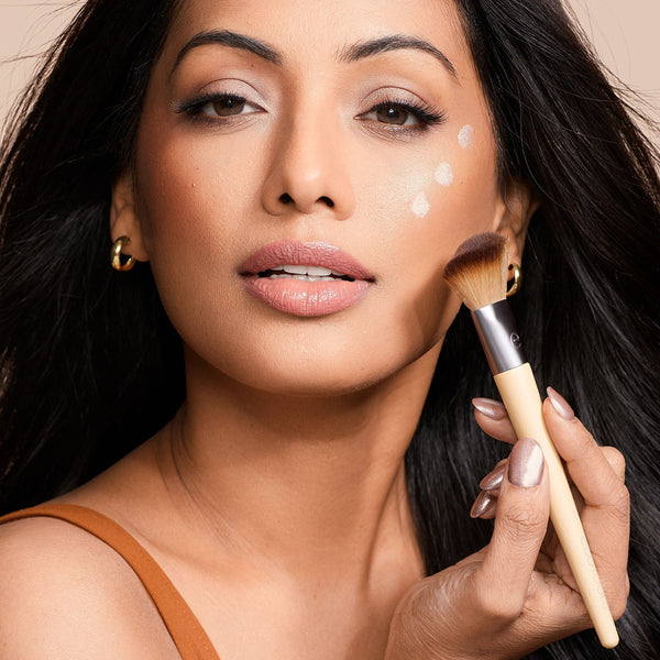Woman applying makeup blush and highlighting with a tapered brush on cheek and temple