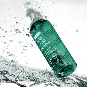 Green brush cleaner bottle with white sprayer, surrounded by water droplets.