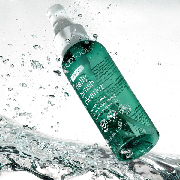 Green brush cleaner bottle with white sprayer, surrounded by water droplets.