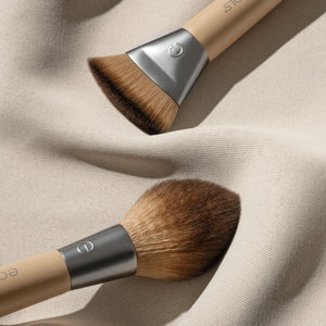 Dual-ended makeup brush on beige cloth, brown bristles and silver ferrules