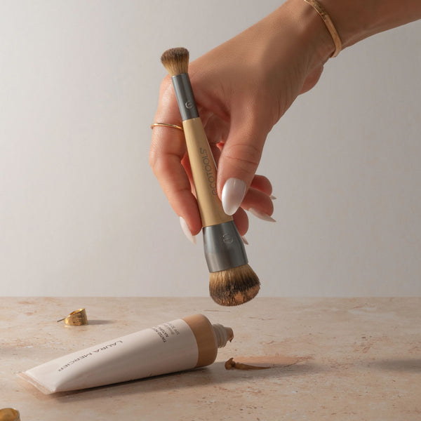 Dual-ended brush held in hand with beige handle and brown bristle heads
