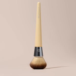 Blending face brush lying down with rounded brown bristles and light beige handle