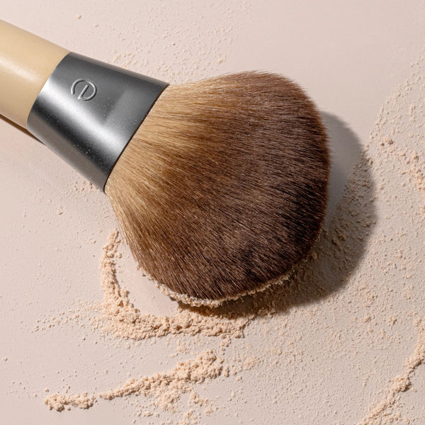 Powder blurring brush with rounded bristle head loaded with beige powder