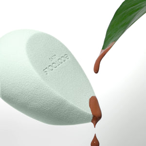 Light green teardrop blurring blender sponge applying brown liquid to skin