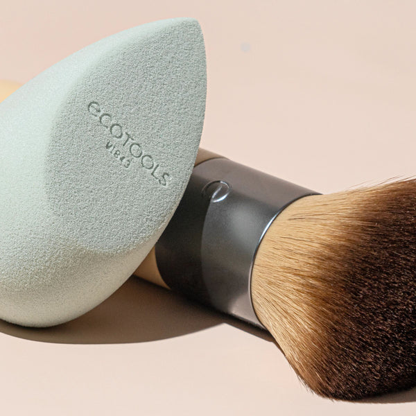 Close-up of mint teardrop blending sponge next to face brush with dark bristles