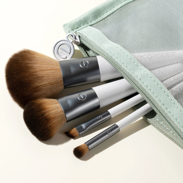 Close-up of 3 makeup brushes with brown bristles and light green zip pouch.