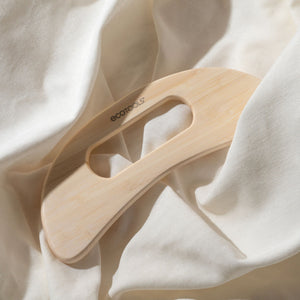 Bamboo wooden body massager resting on soft fabric, curved ergonomic shape and handle slot.