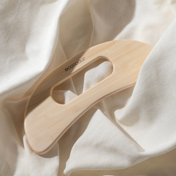 Bamboo wooden body massager resting on soft fabric, curved ergonomic shape and handle slot.