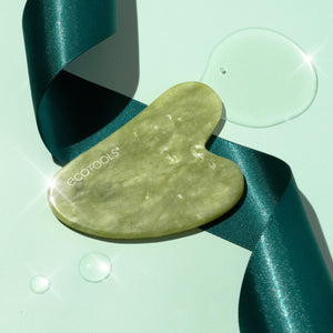 Heart-shaped light green jade face tool beside teal satin ribbon