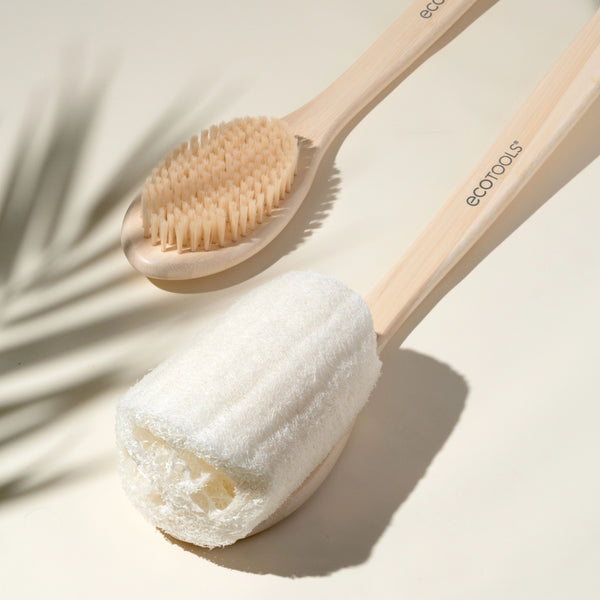 Bath brush with oval bristle head and bamboo handle resting on a soapy towel.