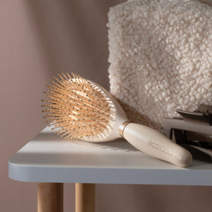Detangling hair brush on a ledge with light wood handle and pin bristles