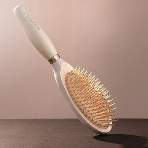 Light wood oval hair detangling brush with mixed-length pins on a curved handle