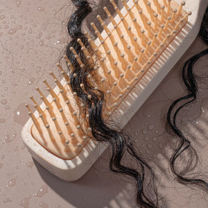 Detangling brush brushing through wet dark curls with visible droplets
