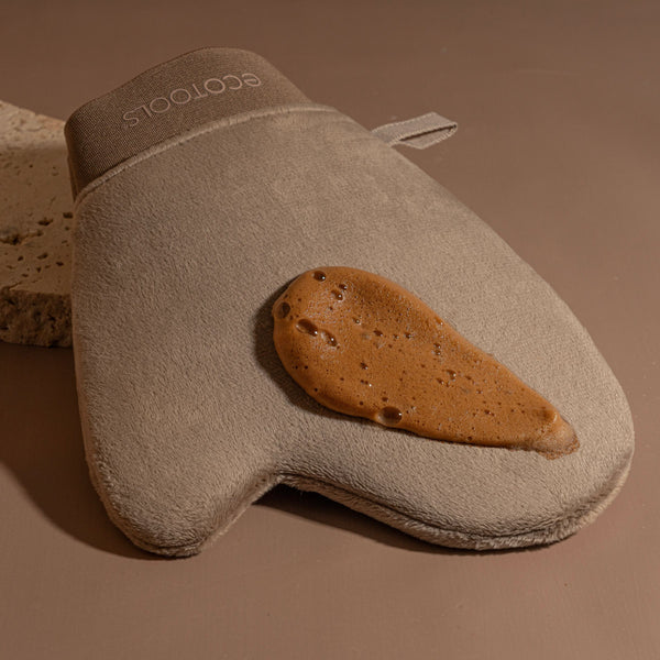 Beige tanning mitt holding self-tanner on the application surface
