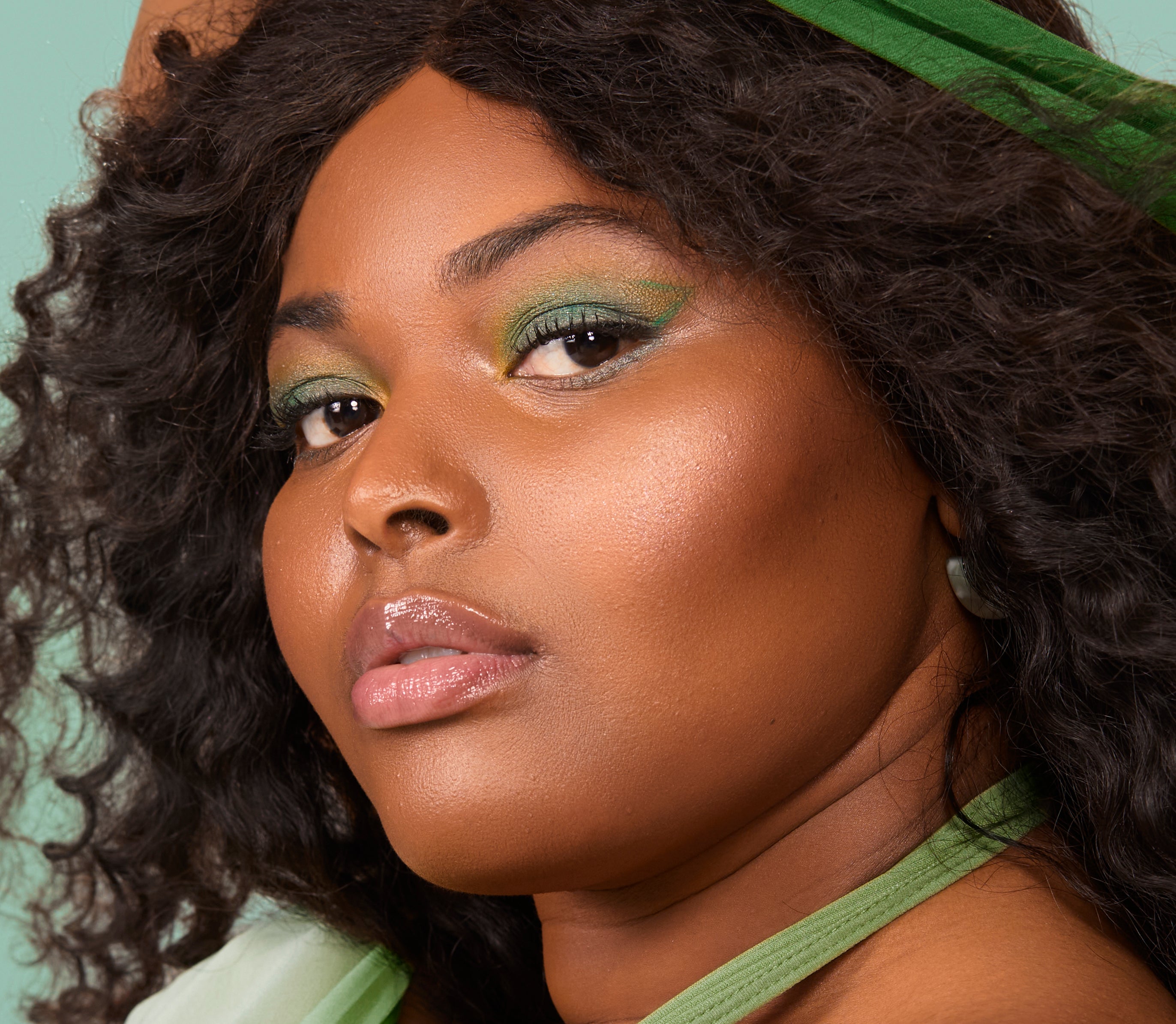 Close up portrait of a woman with dark curly hair, green eyeshadow, and a green headband