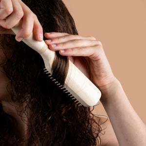 White detangling paddle brush styling curly hair while hands grip handle and comb through