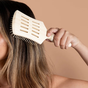 White paddle hair brush detangling with a hand near the scalp
