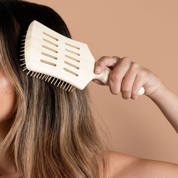 White paddle hair brush detangling with a hand near the scalp