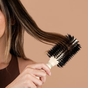 Round hair volumizing brush with white handle and black bristles, held in hand