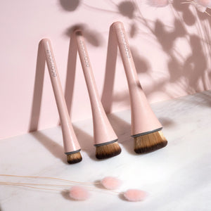 Three makeup brushes standing together, pink handles with black ferrules and golden bristle tips