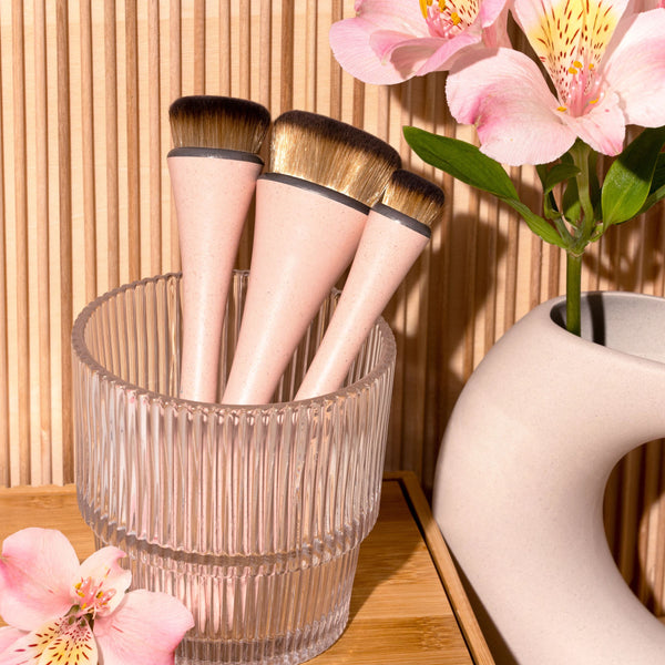 Makeup brush set in a clear cup, three pink-handled brushes with golden bristles