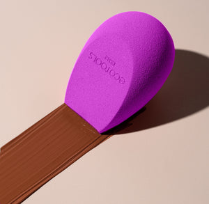 Purple teardrop makeup sponge angled on a makeup brush handle