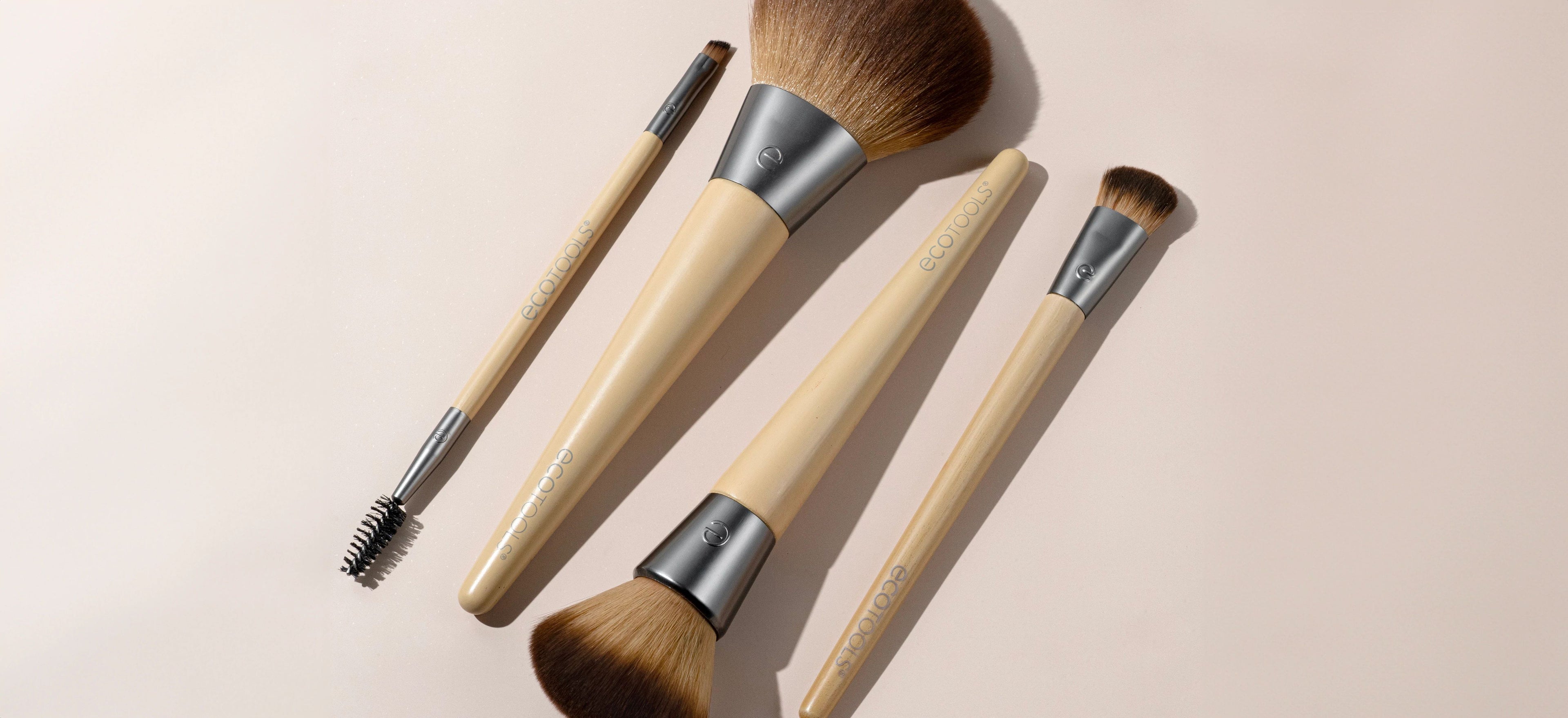 Makeup brushes with beige handles and brown bristles, arranged on a light pink background