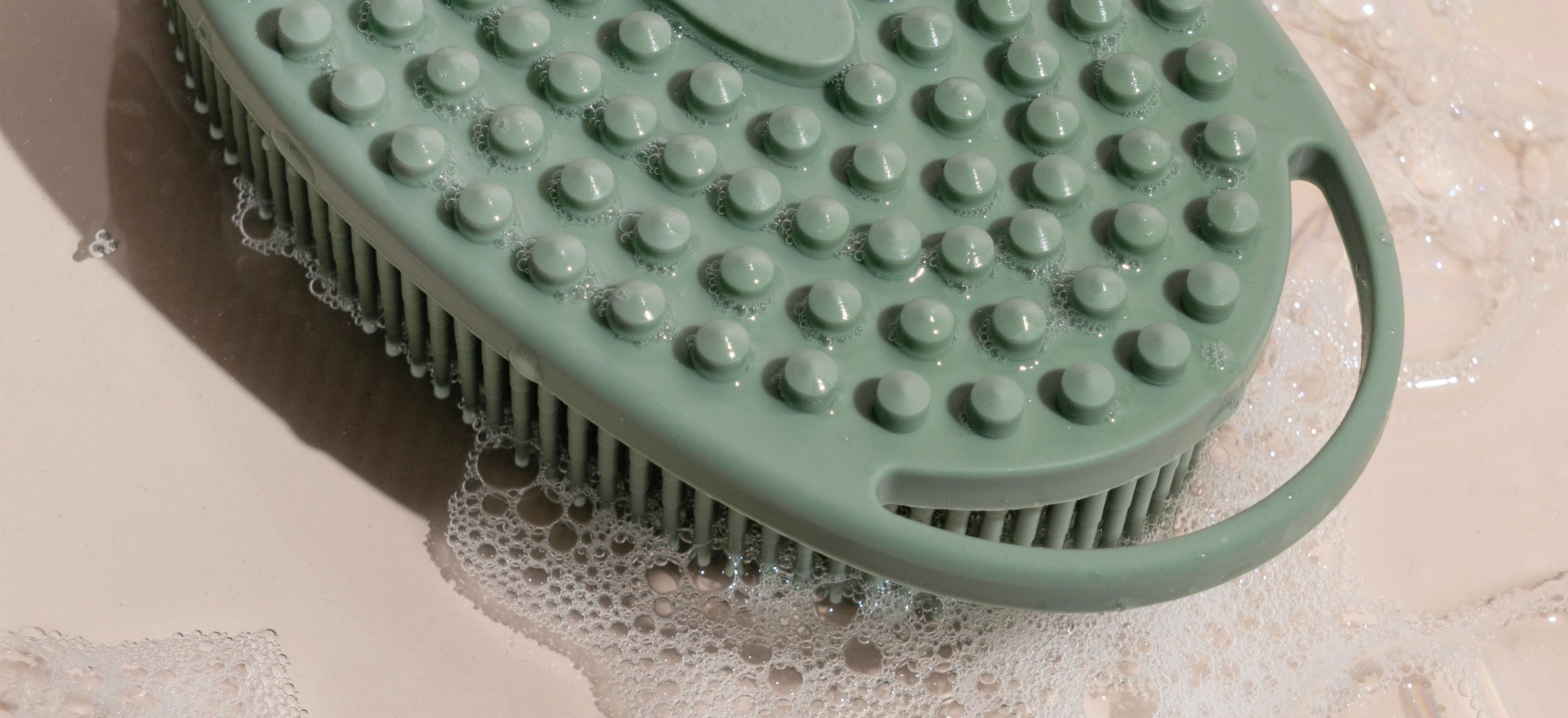 Mint green plastic brush head with rows of round bristles and soap bubbles on a white surface