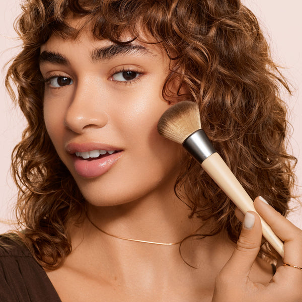 Blending face brush applying makeup on a model’s cheek with soft rounded bristle head