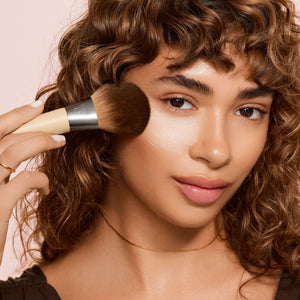 Makeup brush sweeping powder on face; dark bristles on light bamboo handle