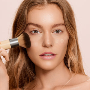 Person applying makeup with a face brush, dark bristles and bamboo handle
