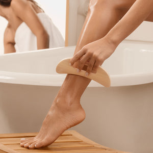 Wooden body massager being used on the leg over the bathtub edge, curved bamboo tool.