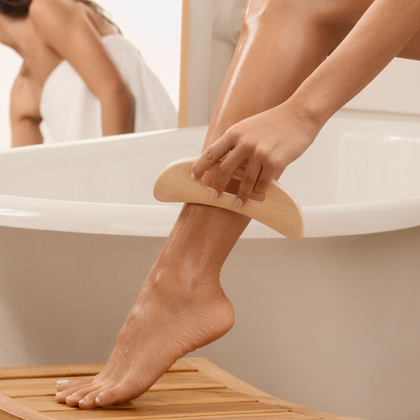 Wooden body massager being used on the leg over the bathtub edge, curved bamboo tool.