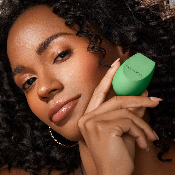 Green teardrop makeup sponge held near a person’s face for applying foundation.