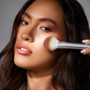 Cheek highlight brush with silver handle and brown bristles applying shimmer makeup