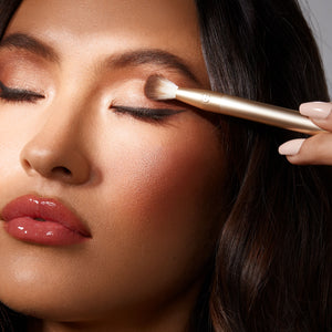 Woman applying shimmer eye makeup with a gold angled brush near the lash line.