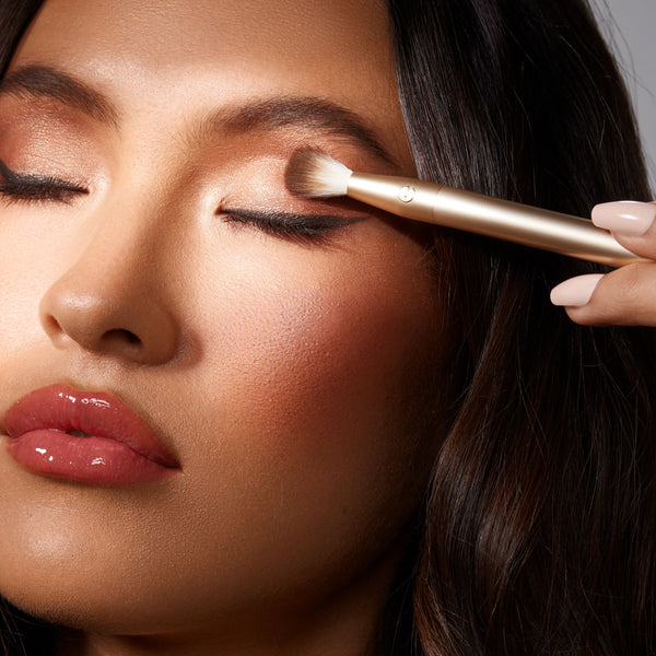 Woman applying shimmer eye makeup with a gold angled brush near the lash line.