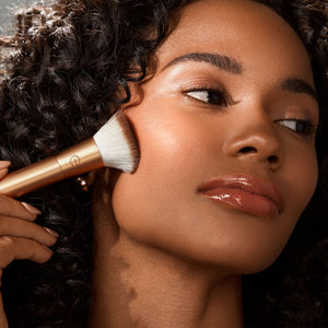 Large makeup blending brush buffing product onto cheek for an even finish.