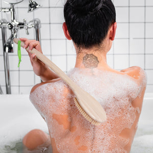 Bath brush with light wooden handle and firm bristles, used on a soapy back.