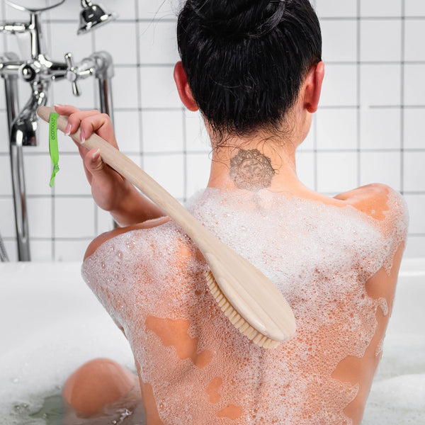 Bath brush with light wooden handle and firm bristles, used on a soapy back.