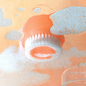 Mini cleansing brush releasing foamy cleanser as the orange head is scrubbed