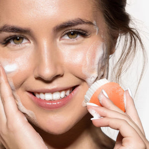 Mini cleansing brush used on face near cheeks and under-eye area, orange head visible