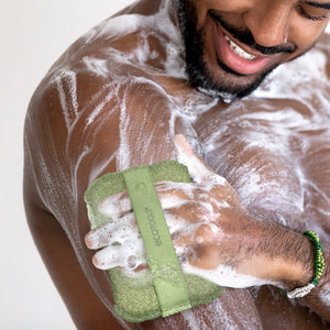 Olive-green exfoliating body buffer in foamy soap during shower use
